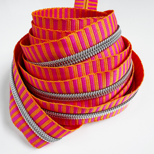 Number 5 continuous zipper tape featuring a bright pink and orange jacquard woven stripe pattern with metallic silver coil teeth, coiled neatly against a white background.