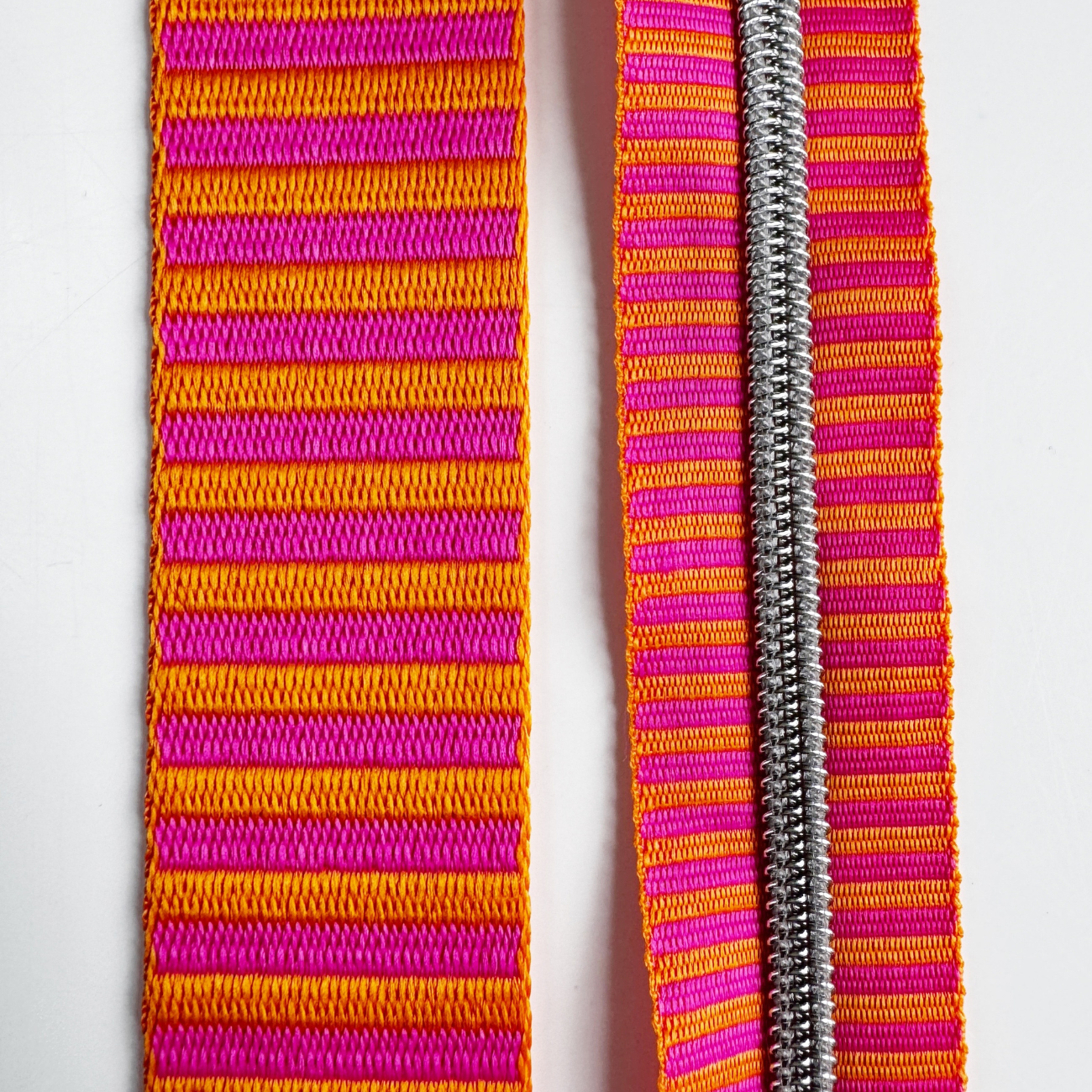A matching bag making set featuring a thick jacquard woven webbing strap on the left and a continuous zipper tape with metallic silver coil teeth on the right, both showcasing an identical bright pink and orange horizontal stripe pattern.
