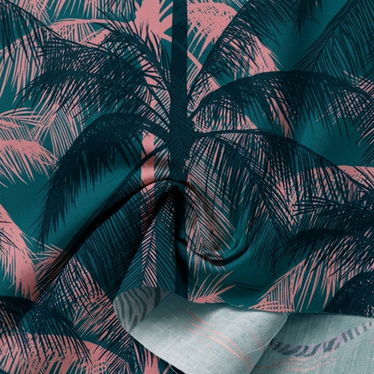 Dark blue tropical palm print cotton fabric by Ruby Star Society, shown in a soft draped close-up featuring layered teal and blush pink palm leaves with a flowing texture perfect for quilting, apparel, bags, and tropical-inspired sewing projects.