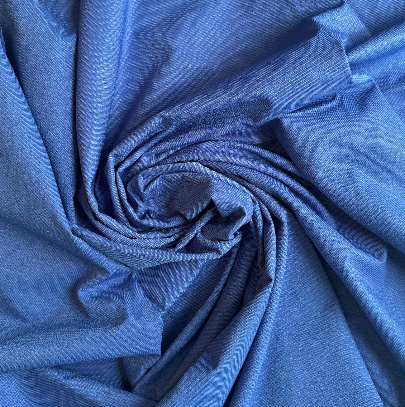 A close-up, top-down view of the royal blue nylon bag lining fabric, artistically arranged in a tight swirl or rosette shape. The lighting highlights the fine, woven, water-resistant texture of the material along the edges of its deep, dramatic folds.