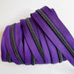 A close-up view of the purple zipper tape neatly layered and wrapped flatly to showcase several parallel rows of the metallic teeth. The shot emphasizes the rich texture of the purple woven fabric tape and the colorful iridescent shimmer on the gunmetal zipper teeth