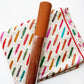 A roll of brown faux leather material placed diagonally over a folded piece of cream-colored fabric printed with colorful feather patterns.