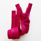 Giant chunky zipper with plastic teeth and oversized circular ring pull on a white background in vibrant, saturated pinkish-red.