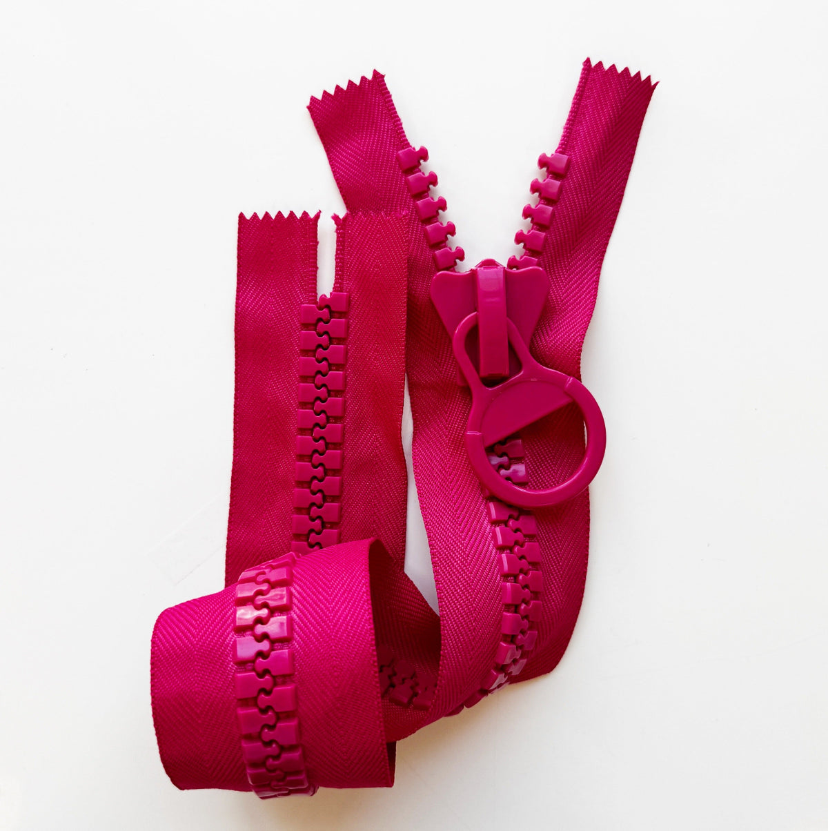 Giant chunky zipper with plastic teeth and oversized circular ring pull on a white background in vibrant, saturated pinkish-red.