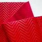 A close-up of a folded red fabric or material sample with a raised chevron pattern, shown against a plain white background.