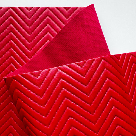 A close-up of a folded red fabric or material sample with a raised chevron pattern, shown against a plain white background.