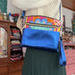 Woman wearing a sweater and skirt, holding a blue and patterned purse.