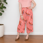 A person standing from the neck down modeling wide-leg cropped pants made from Ruby Star Society Poolside Too Rayon Fabric in Sorbet (Pink). The pants feature a repeating orange and white swimming tiger pattern on a pink background, paired with a solid pink t-shirt and brown ballet flats.