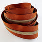 #5 continuous rust orange zipper tape with shimmering gold coil teeth for bag making and upholstery.