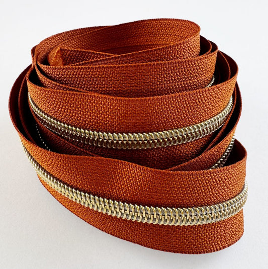 #5 continuous rust orange zipper tape with shimmering gold coil teeth for bag making and upholstery.