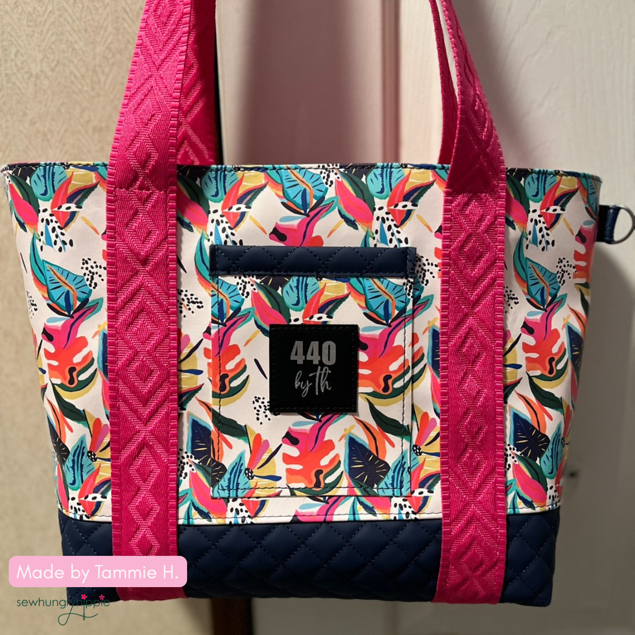 Close-up of a handmade tote bag featuring a bright tropical monstera leaf print canvas, a navy blue quilted diamond faux leather base and pocket trim, a black square '440 by th' brand label, and hot pink geometric diamond jacquard webbing straps