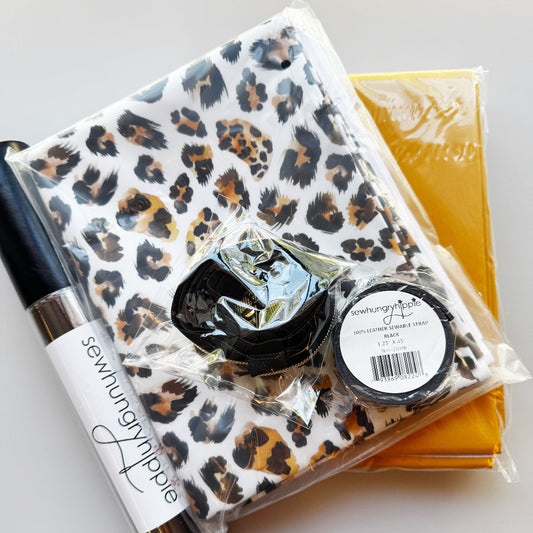 A sewing kit bundle containing a leopard print fabric package, a black sewing machine needle, a black elastic loop, and a yellow mesh bag, all in clear plastic wrapping with a SewhungryNipple brand label visible.
