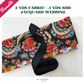 A sewing bundle featuring a folded vibrant floral fabric with red roses, blue blossoms, and multi-colored paisley borders on a black background, paired with a bundled roll of black jacquard woven webbing strap displaying a raised diamond geometric pattern.