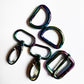 Five metallic carabiner-style keyring clips with a glossy iridescent rainbow finish, arranged on a plain white background.
