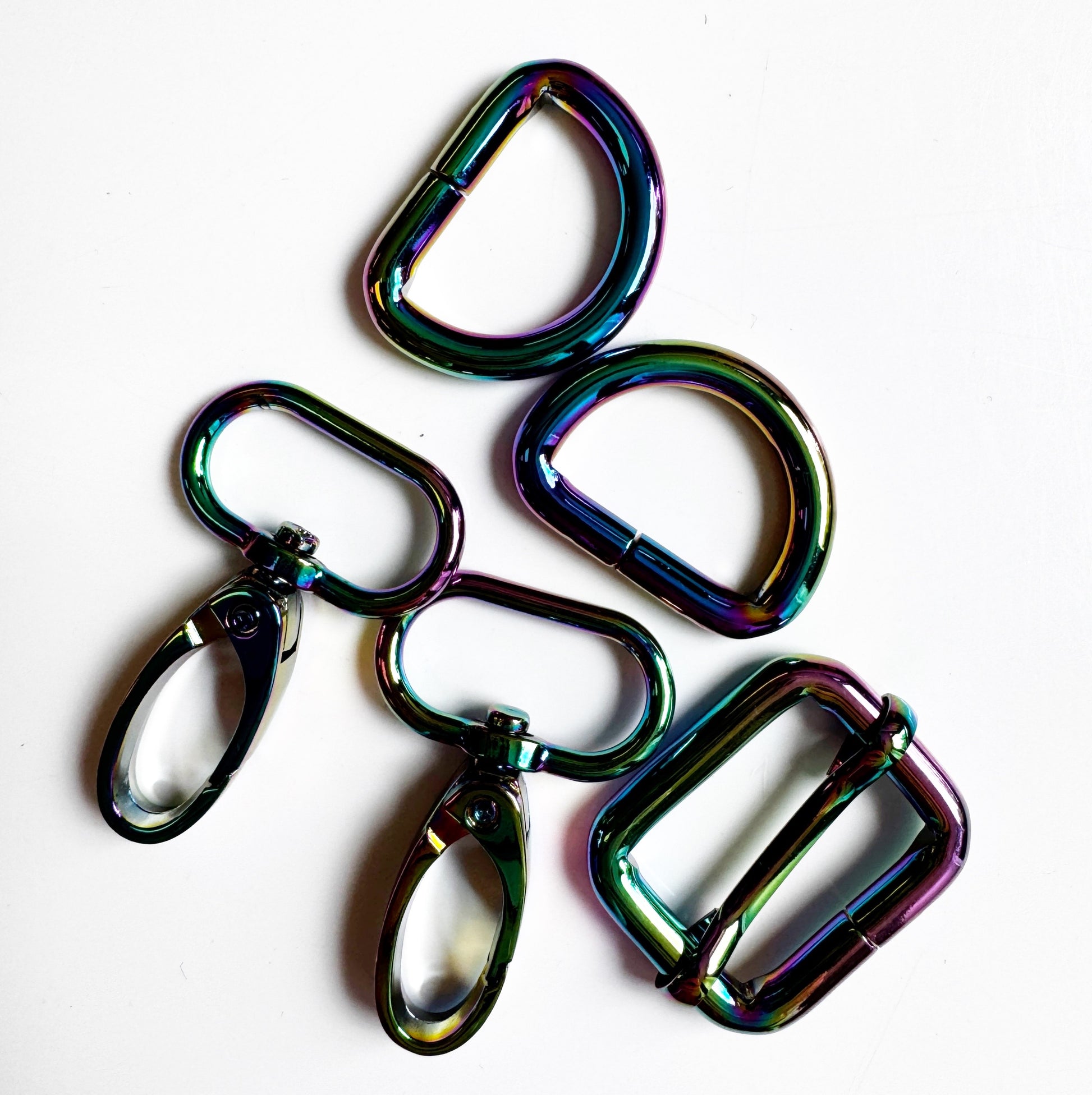 Five metallic carabiner-style keyring clips with a glossy iridescent rainbow finish, arranged on a plain white background.