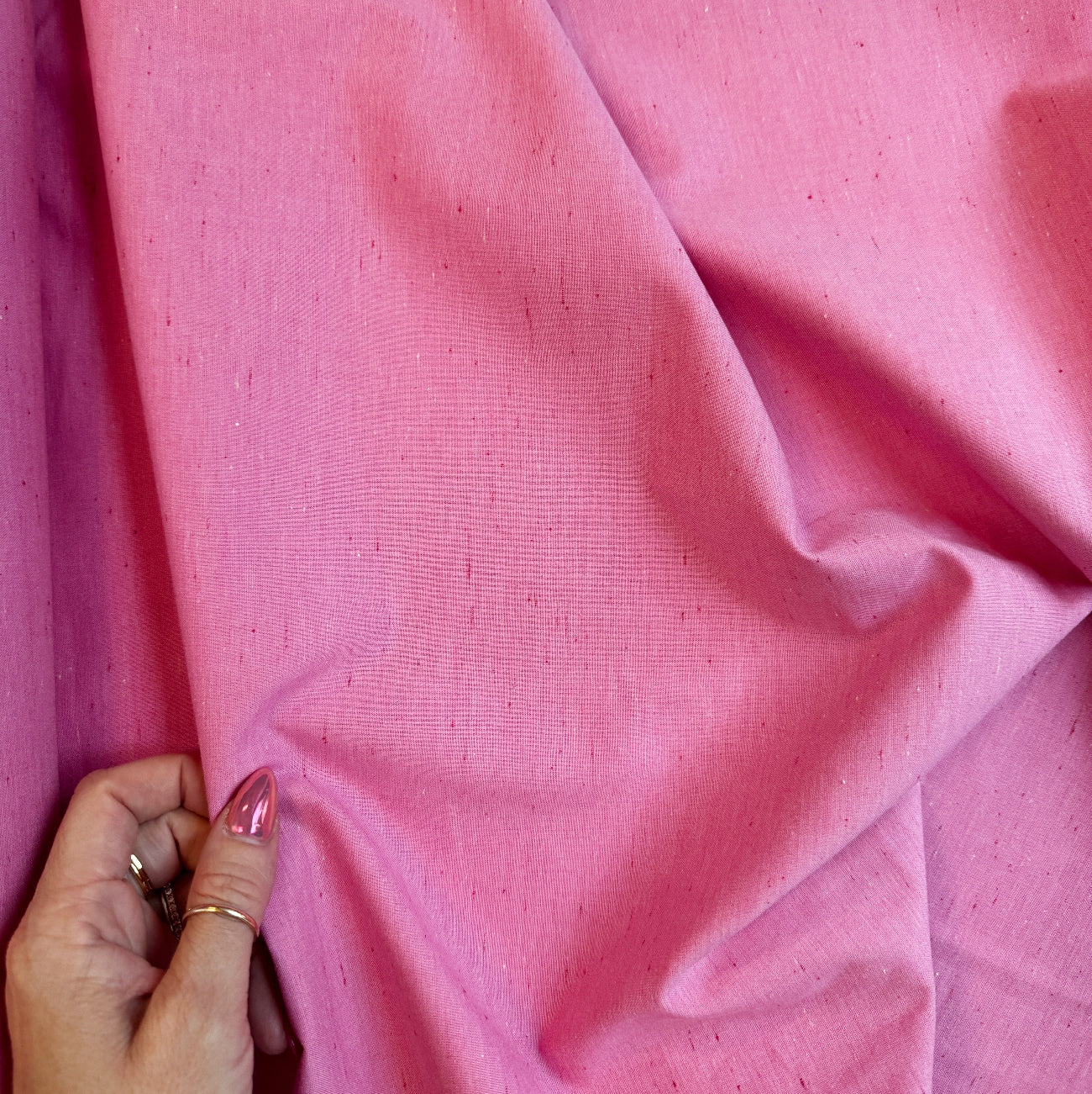 Hand holding a speckled in Bubblegum yarn-dyed woven 100% cotton fabric with textured pink specks for sewing and quilting.
