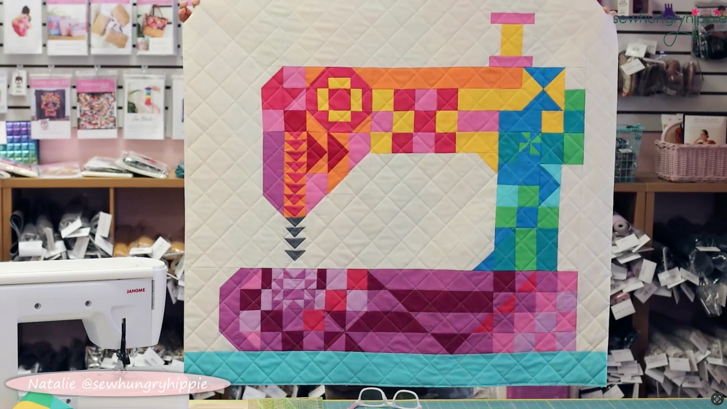 Natalie holding up a colorful quilt with geometric blocks in the shape of a sewing machine in the Sew Hungry Hippie sewing studio