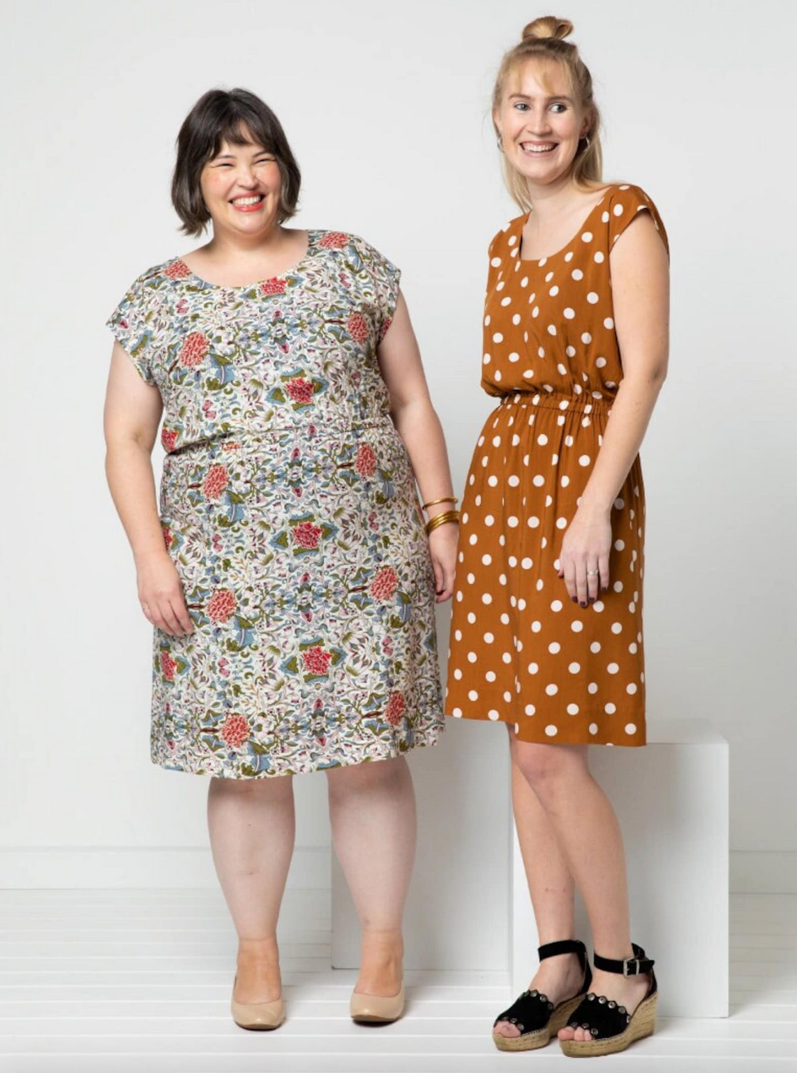 Two women wearing dresses standing against a white background
