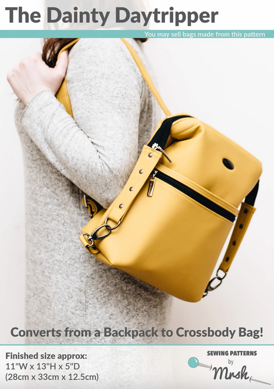 Yellow crossbody bag held by a person wearing a gray sweater on a white background. The Dainty Daytripper sewing pattern cover