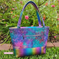 Santorini Tote bag in Iridescent rainbow  featuring a watercolor galaxy print fabric, textured metallic base, and rainbow zipper hardware.