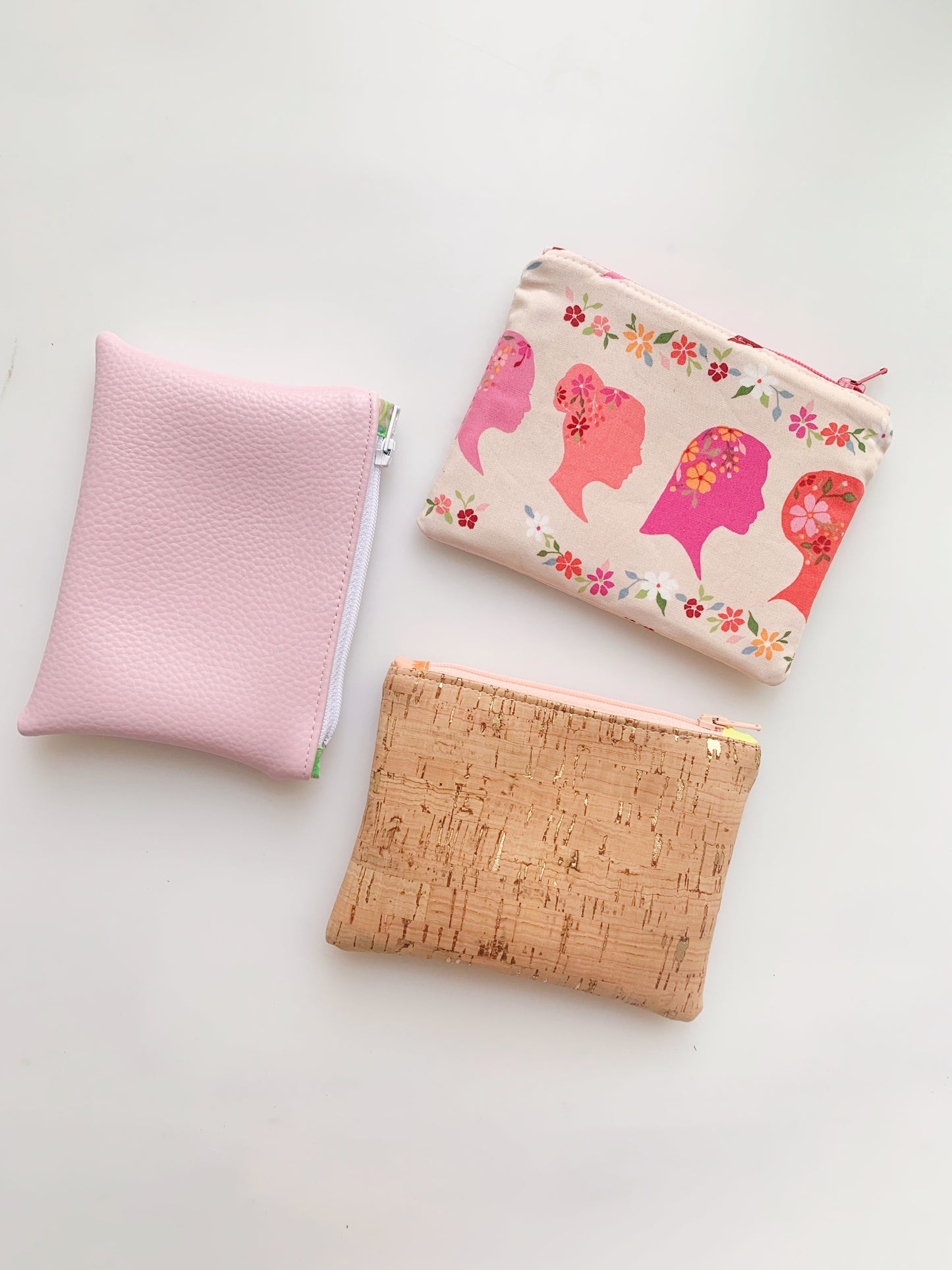 Three stylish coin purses in pink, floral, and cork designs.