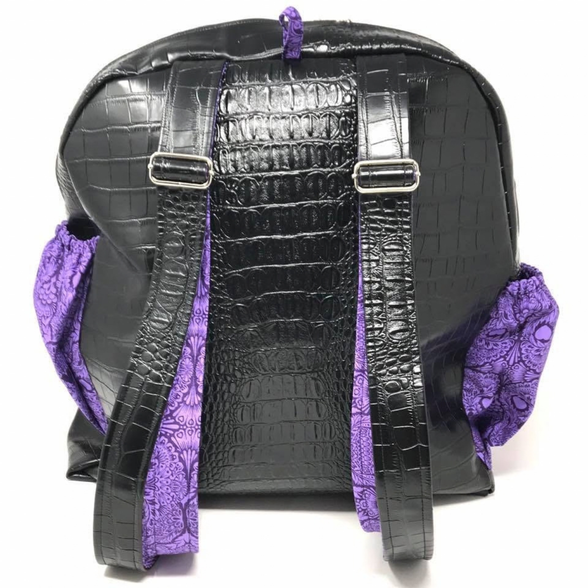 Back view of black croc-embossed Trina Backpack showing adjustable shoulder straps and purple side pockets
