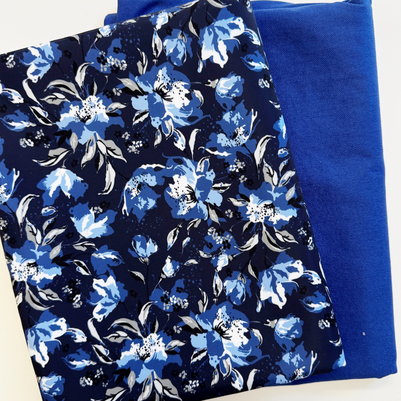 A coordinated fabric bundle for bag making featuring two folded materials: a dark navy blue bonded nylon exterior fabric printed with a vibrant blue, white, and gray floral pattern, paired with a matching solid bright royal blue polycotton lining fabric.