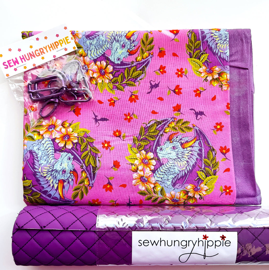 A folded fabric sewing pattern book or pattern set on a white background, featuring a bright pink cover with a dragon and floral print, a purple quilted envelope-style cover, and a branded label reading 'sewhungryhippie'.