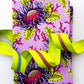 A folded fabric item, likely a napkin or small table linen, featuring a vibrant purple and lime green floral pattern with a bright neon yellow-green ribbon threaded through it, set against a plain white background.
