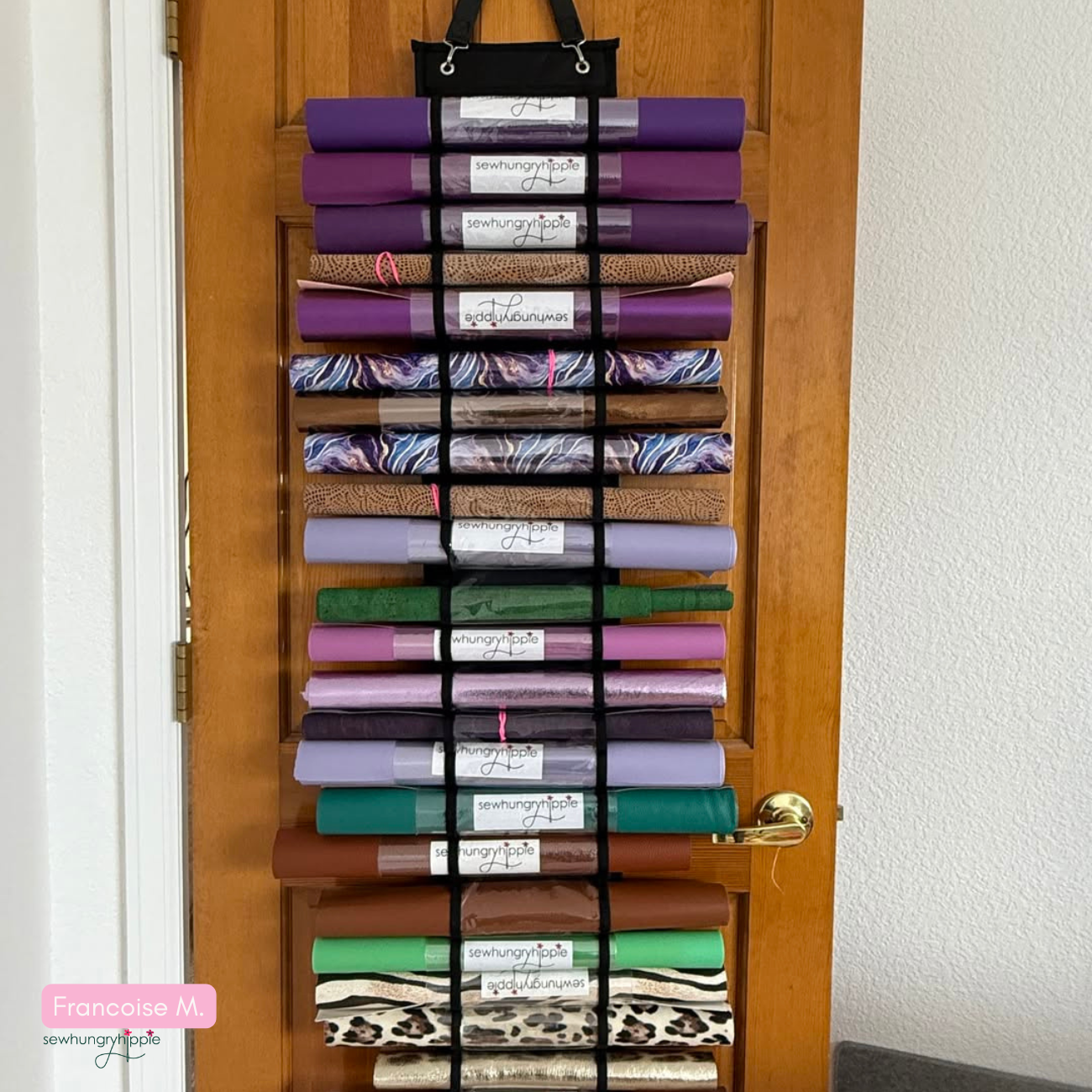Vinyl organizer hanging on a wooden door, featuring numerous horizontal pockets filled with rolled vinyl in various colors and prints