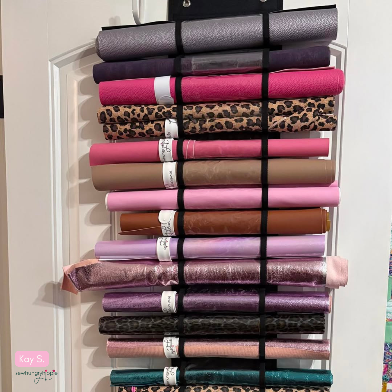 Vinyl organizer hanging on a wooden door, featuring numerous horizontal pockets filled with rolled vinyl and cork in various colors and prints