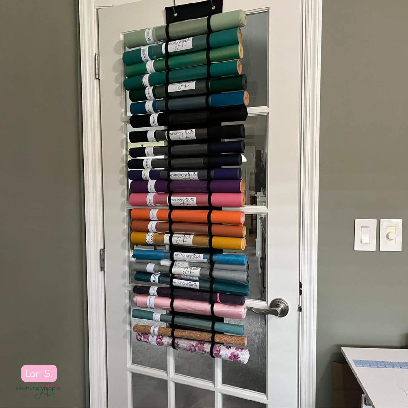 Vinyl organizer hanging on a wooden door, featuring numerous horizontal pockets filled with rolled vinyl in various colors and prints