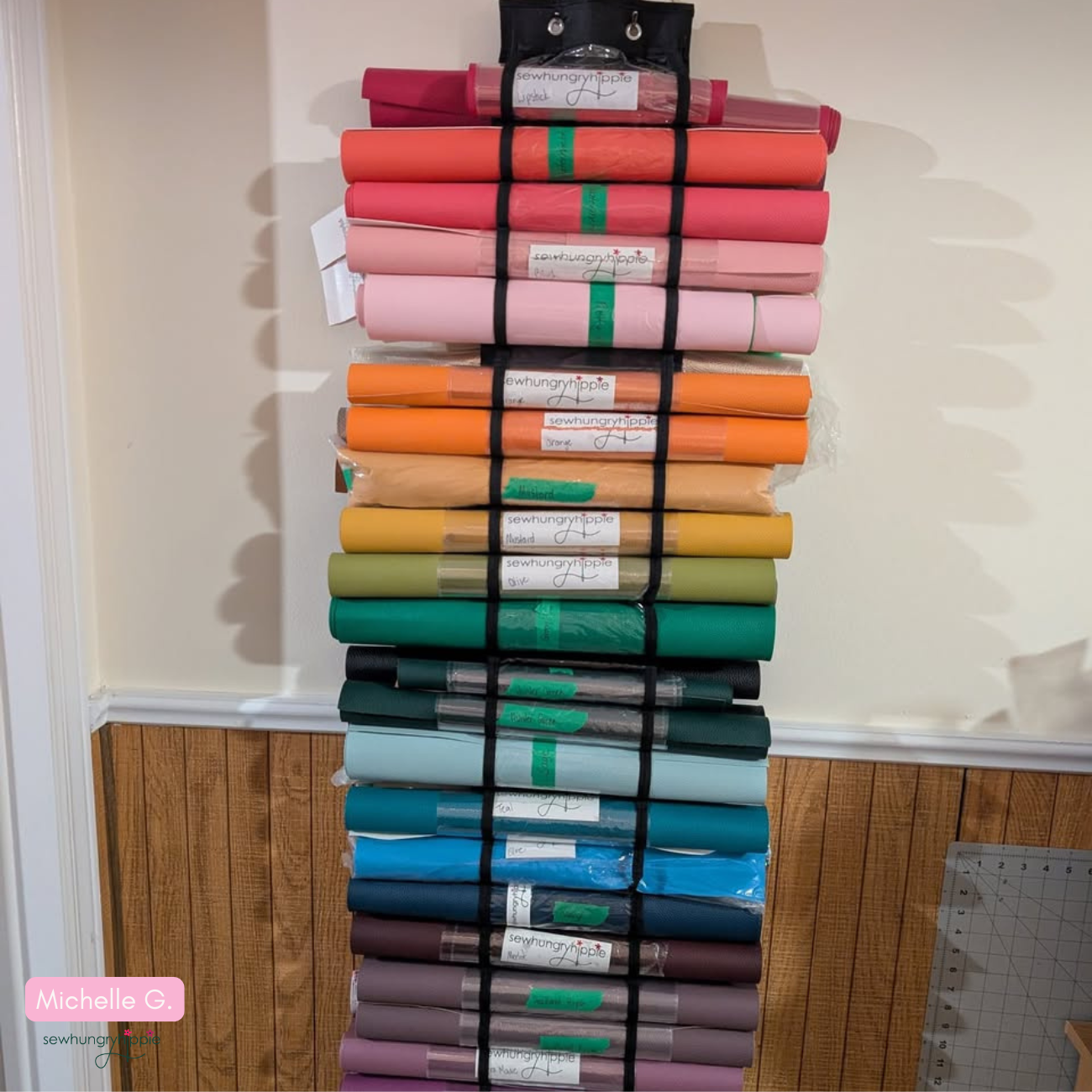 Vinyl organizer hanging on a wooden door, featuring numerous horizontal pockets filled with rolled vinyl in various colors and prints