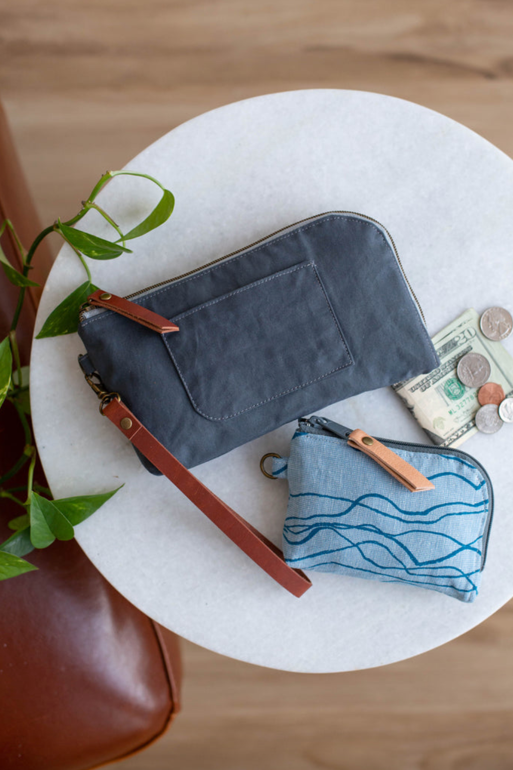 Two small blue wallets on a round white table with a plant in the background.