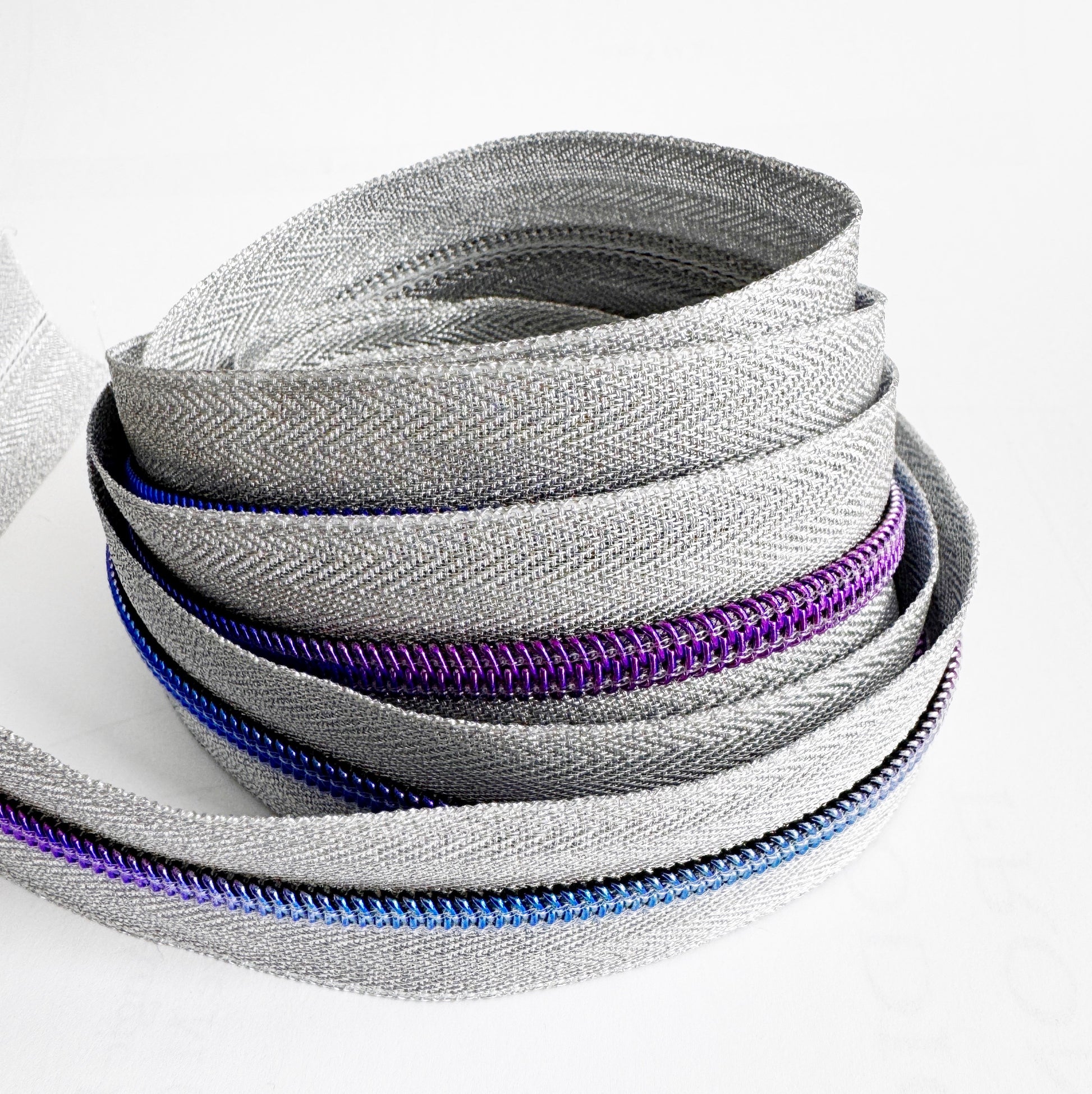 Stack of gray silver zipper tape with purple and blue teeth on a white background