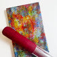 A vibrant abstract multi-colored fabric with halftone dot patterns paired with a roll of red cork fabric.