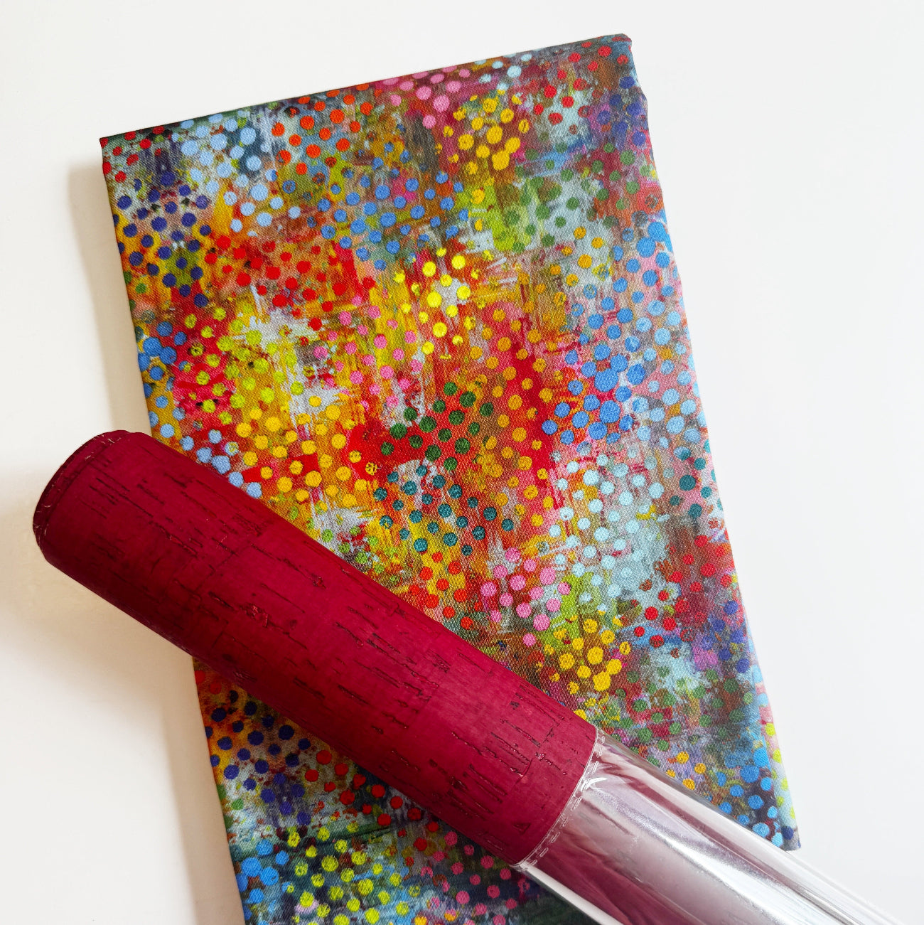 A vibrant abstract multi-colored fabric with halftone dot patterns paired with a roll of red cork fabric.