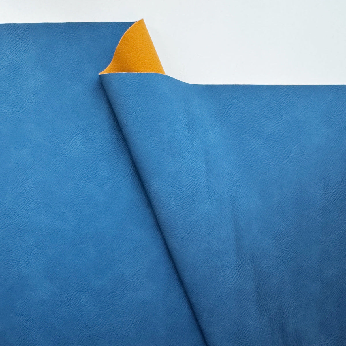 Blue faux leather vinyl fabric with a soft textured surface and contrasting backing, suitable for bag making, purses, upholstery, and sewing projects.