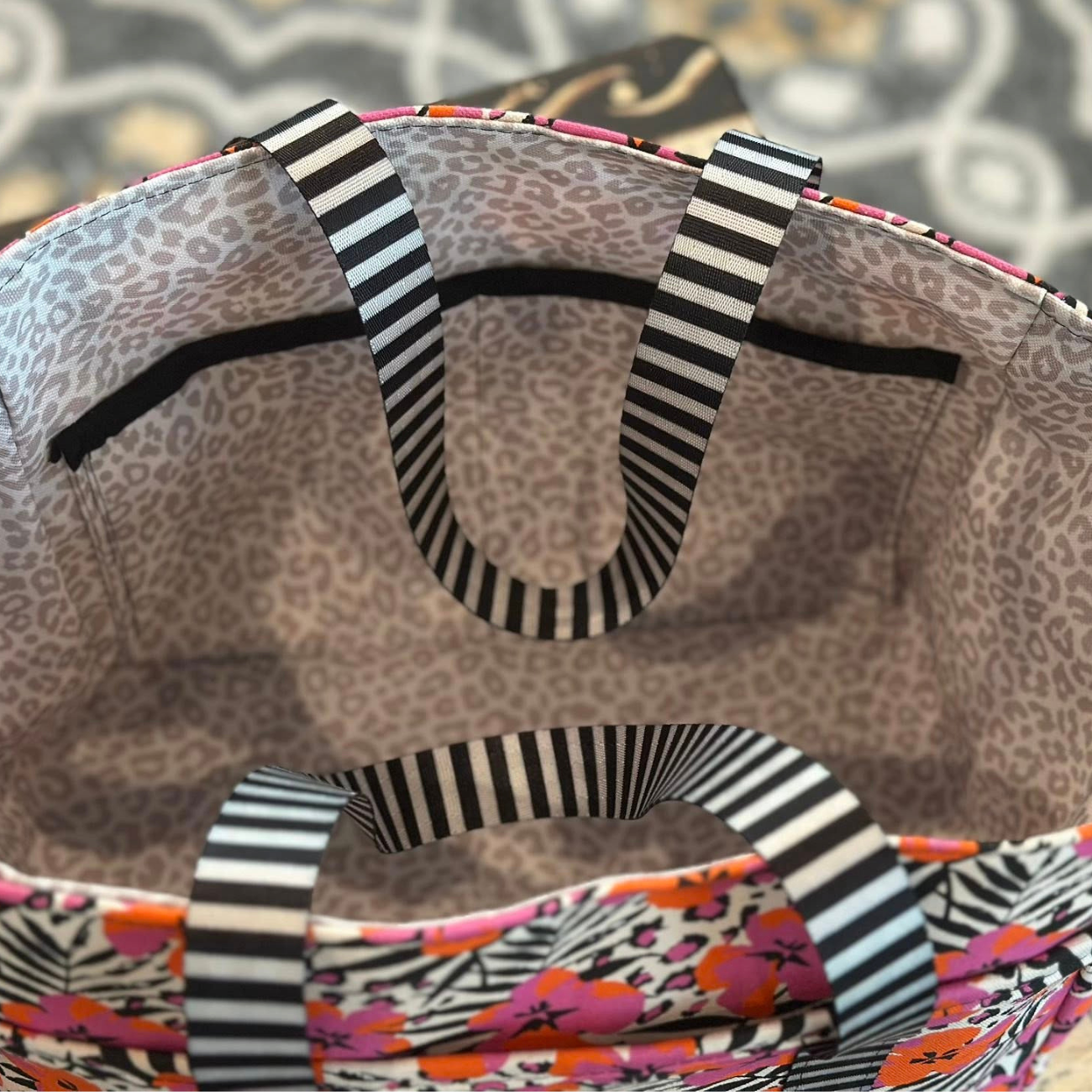 Interior view of a handmade canvas tote bag featuring muted leopard print lining, interior pockets, and black and white striped webbing straps