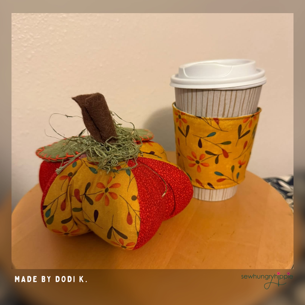 Handmade autumn fabric pumpkin with orange-red and yellow floral panels, matching floral coffee cup sleeve, felt stem, green leaves, and faux moss