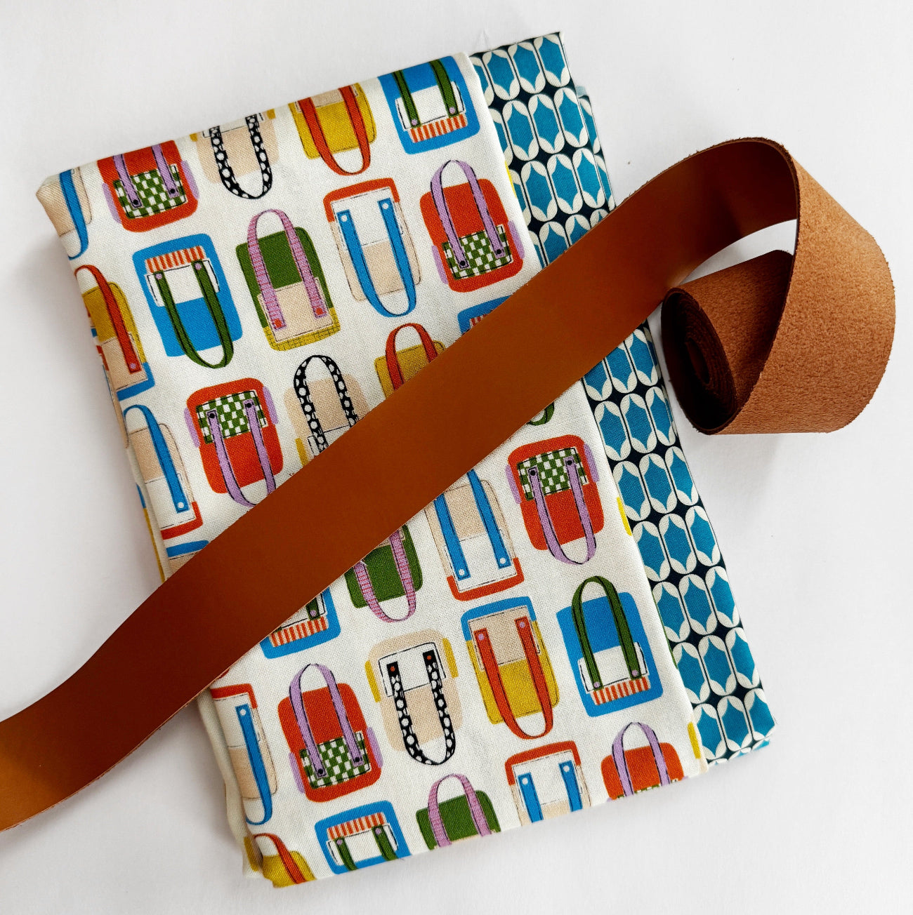 Bag print cotton fabric paired with coordinating blue geometric fabric and cognac leather bag strap for sewing handbags, totes, crossbody bags, and handmade accessories