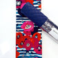 A folded fabric accessory with a navy quilted top and a colorful floral print featuring red, pink, and blue flowers on a striped background, shown next to a clear plastic tube labeled 'sewing'.