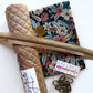 A sewing kit laid out on a white background, including a rolled tan quilted fabric piece, a dark floral fabric panel, a tan zipper, metal clips, and a small branded tag reading 'Sem Hungry Hippie'.