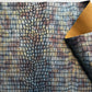 Textured fabric with a pattern resembling crocodile skin, displayed with a yellow corner.
