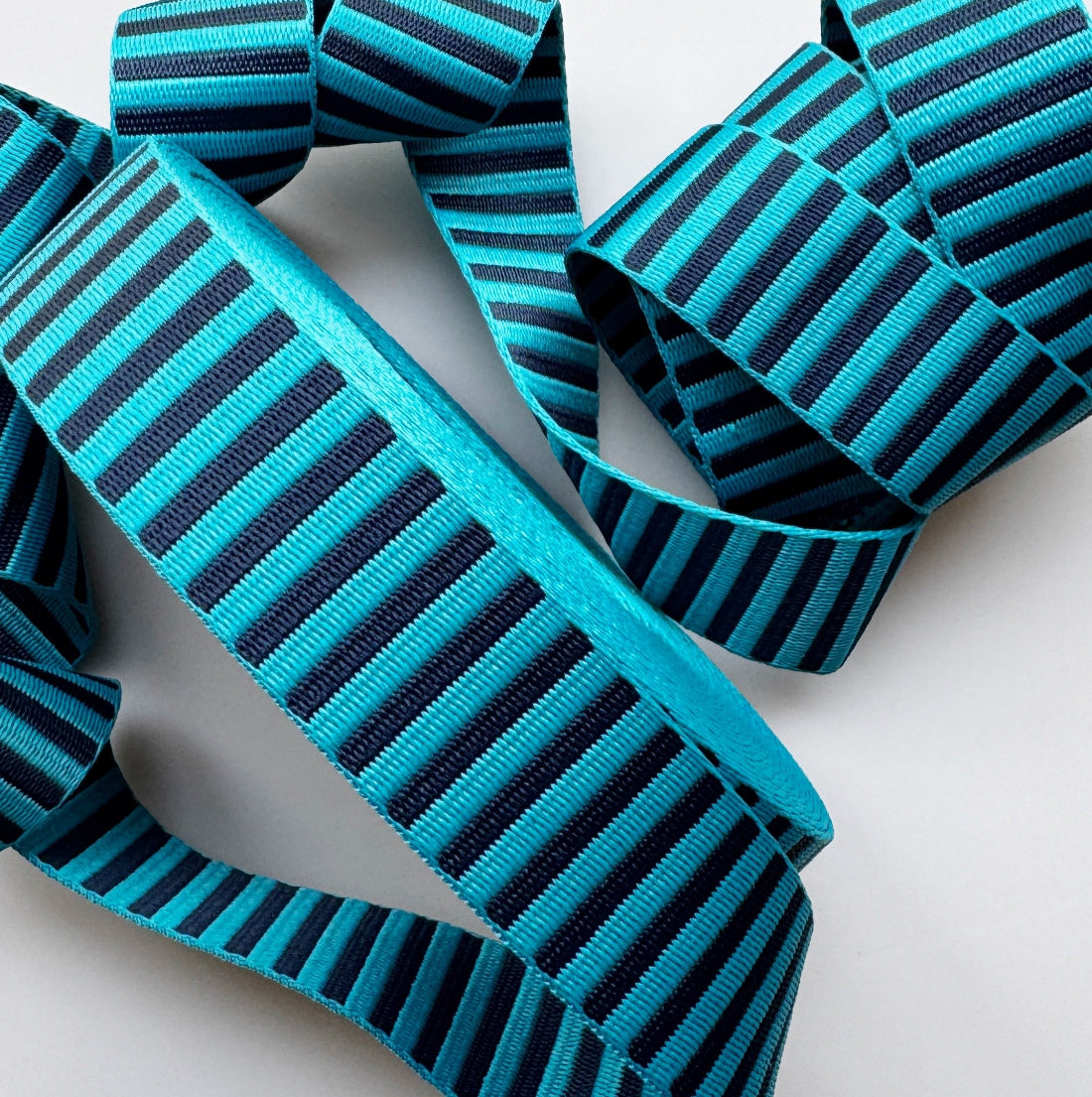 Turquoise and black striped grosgrain ribbon, neatly coiled and arranged on a clean white background.