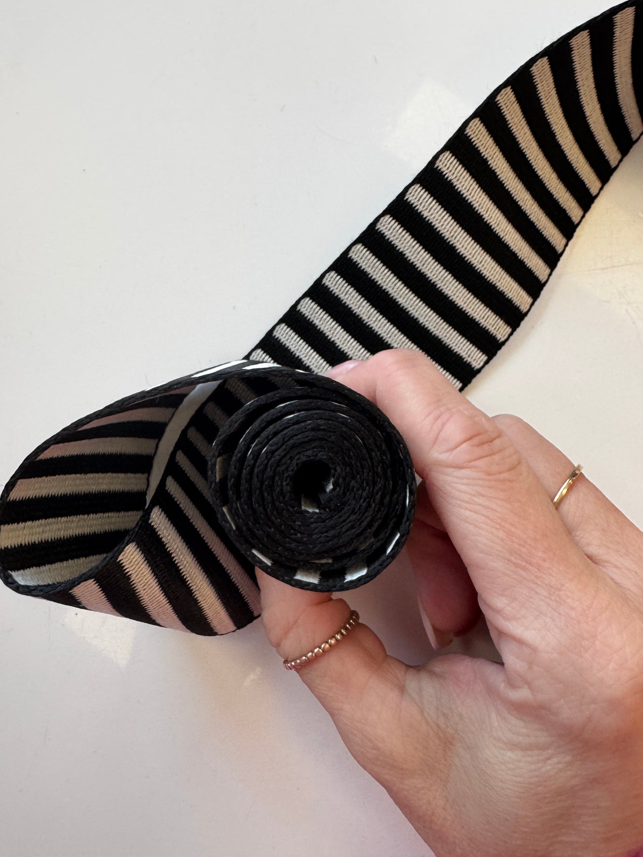 A hand holding a rolled bundle of classic black and white horizontally striped jacquard woven webbing strap for bag making