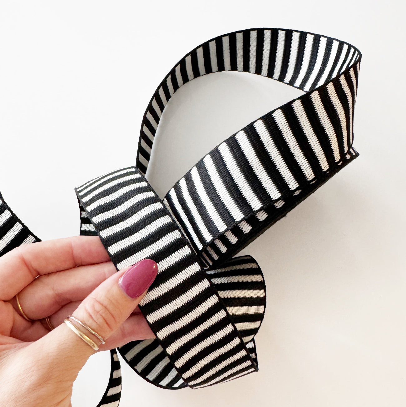 A hand holding a looped section of heavy-duty black and white striped jacquard woven webbing strap on a white background
