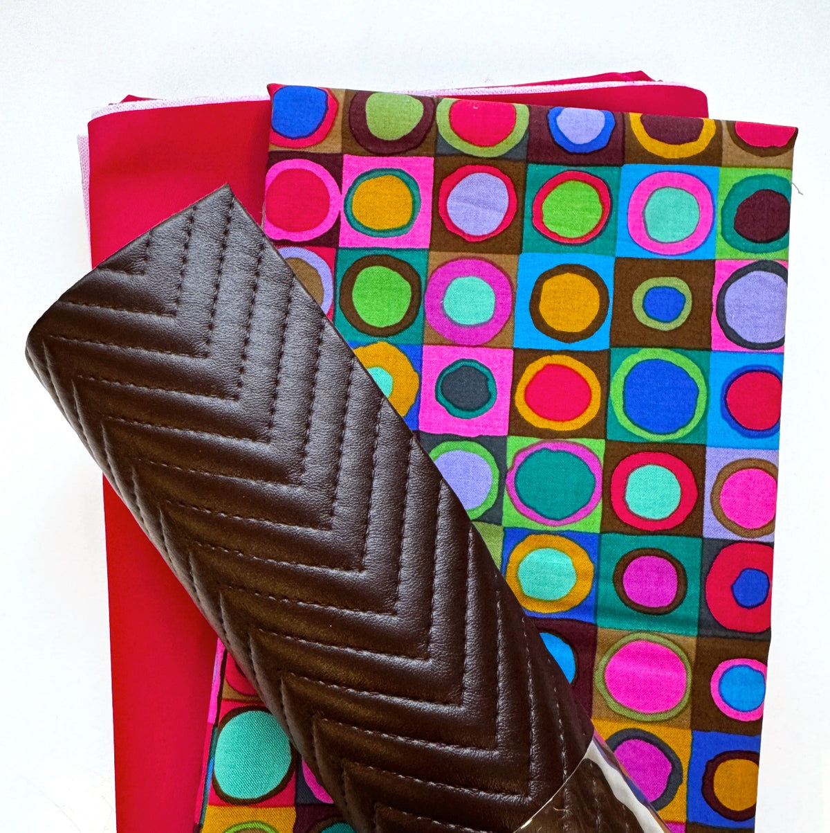 Black chevron-quilted faux leather strap paired with bright pink fabric and colorful retro circle-print fabric for bag making