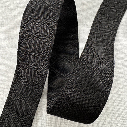 A close-up view of a premium black jacquard woven webbing strap showing a subtle, raised diamond geometric texture on a light gray background 9D44D092