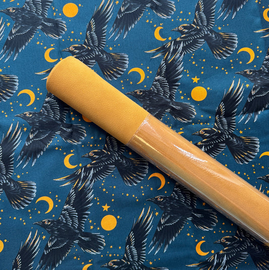 Black raven moon cotton fabric featuring flying ravens, golden moons, and stars paired with a mustard cork fabric roll for bag making and sewing projects.